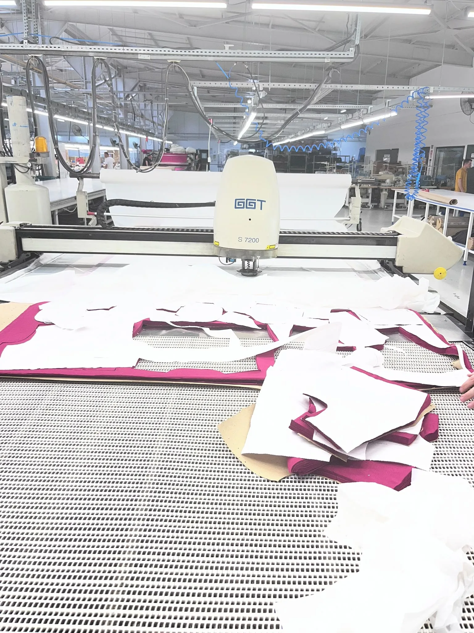 An automatic cutter on a long table, cut pink and white knit panels lying in front of it