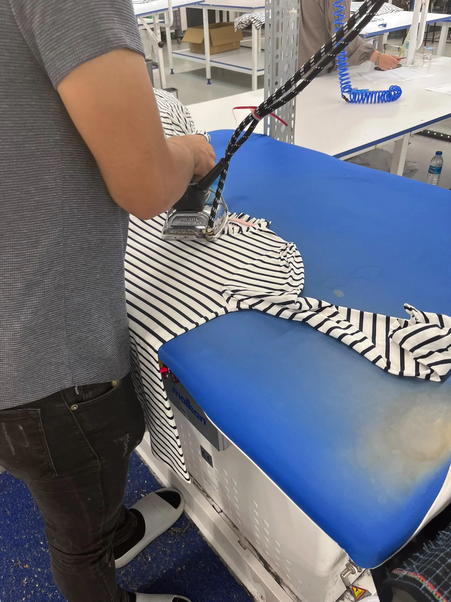 A striped knit being steam-ironed on a blue pressing table