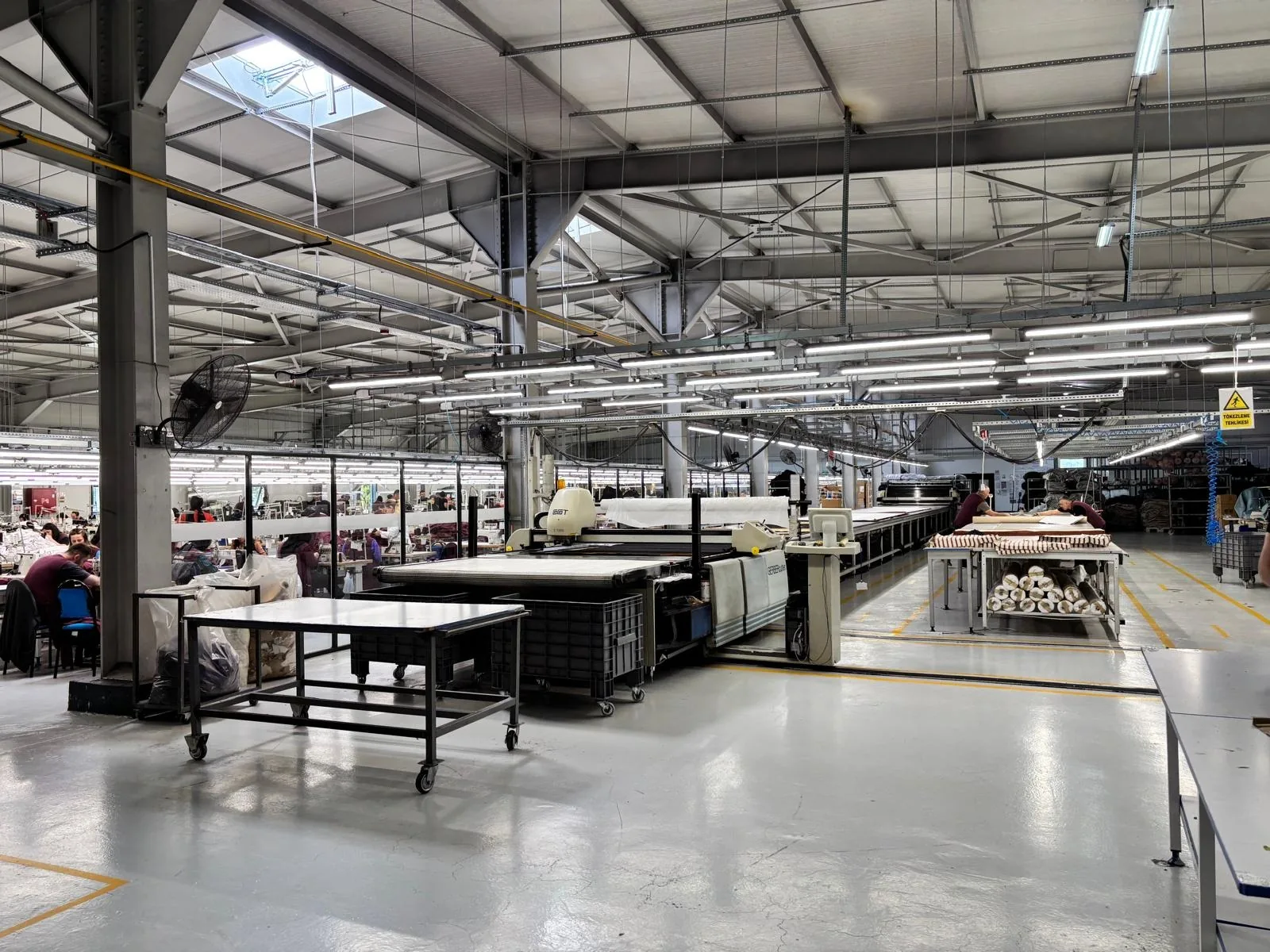 The Erbaa production hall: cutting tables in front, sewing lines behind, under a skylit steel roof