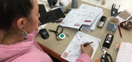 A Darsateks pattern maker working at her desk with tech packs and measurements