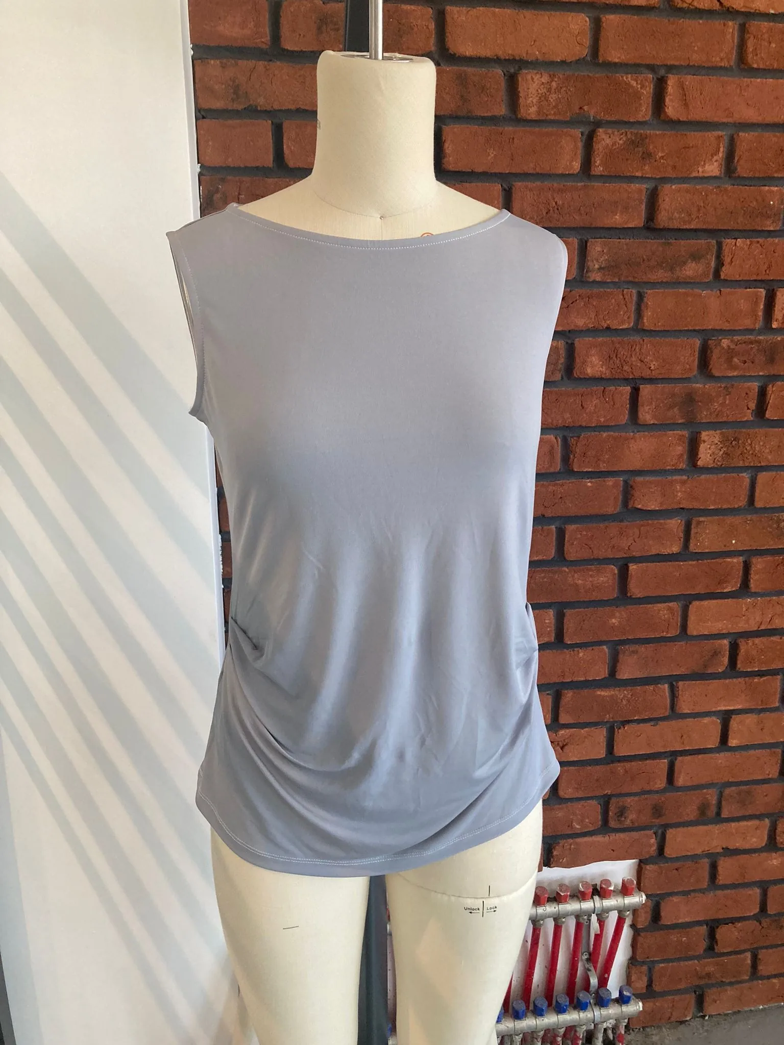 Sample of a grey sleeveless jersey top on a fitting mannequin against a brick wall