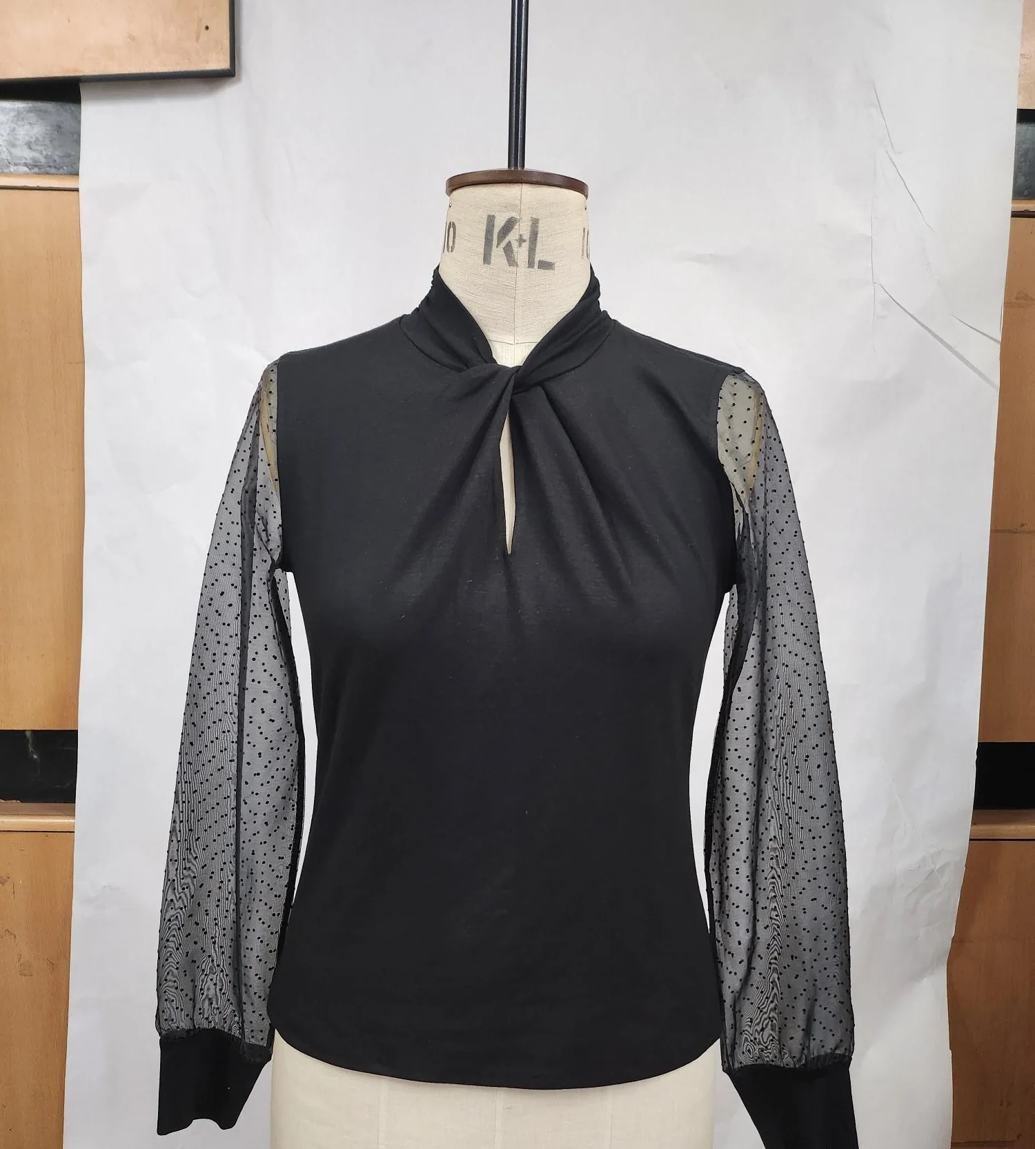 Sample of a black knit blouse with sheer dotted sleeves on a fitting mannequin, made for Karl Lagerfeld