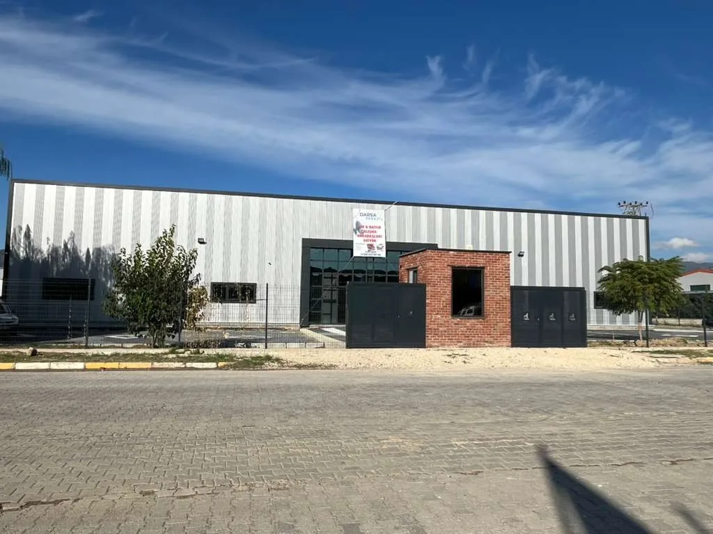 The steel-clad second Darsateks factory in Erbaa with a red-brick gatehouse in front, under a blue sky